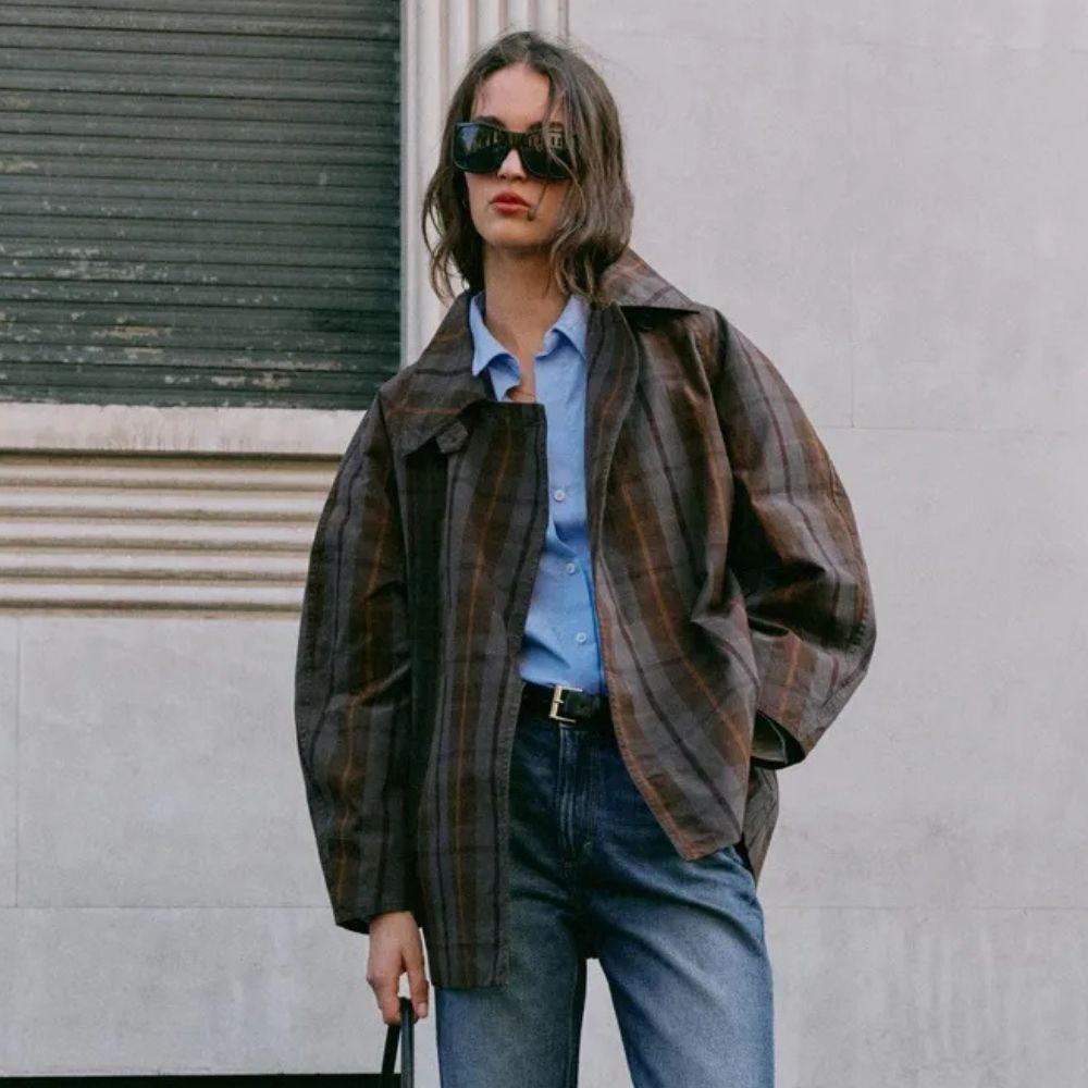 Woman wears check trench coat, blue shirt, blue jeans and black belt