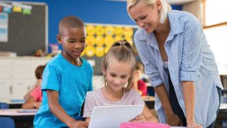 K12 teacher works with two children using an iPad