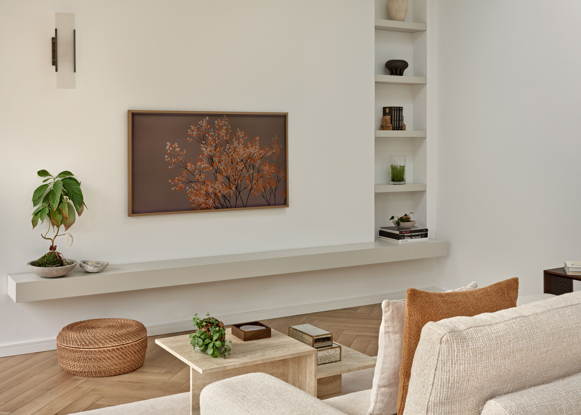 A modern living space with a frame tv picturing blossom that ties in with the natural brown tones in the otherwise neutral space with a coffee table styled with a plant and decorative objects
