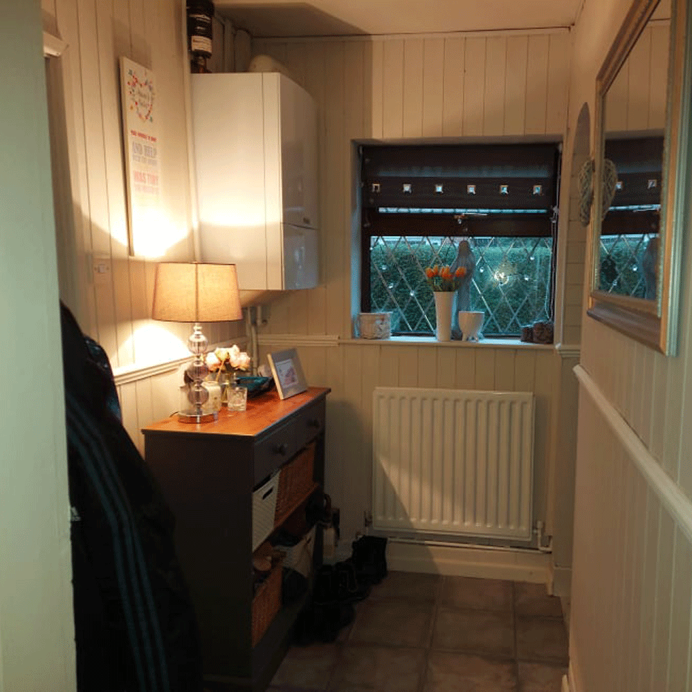 Hallway with chest of drawers with lamp om top next to mounted heater and a window above with a garden view