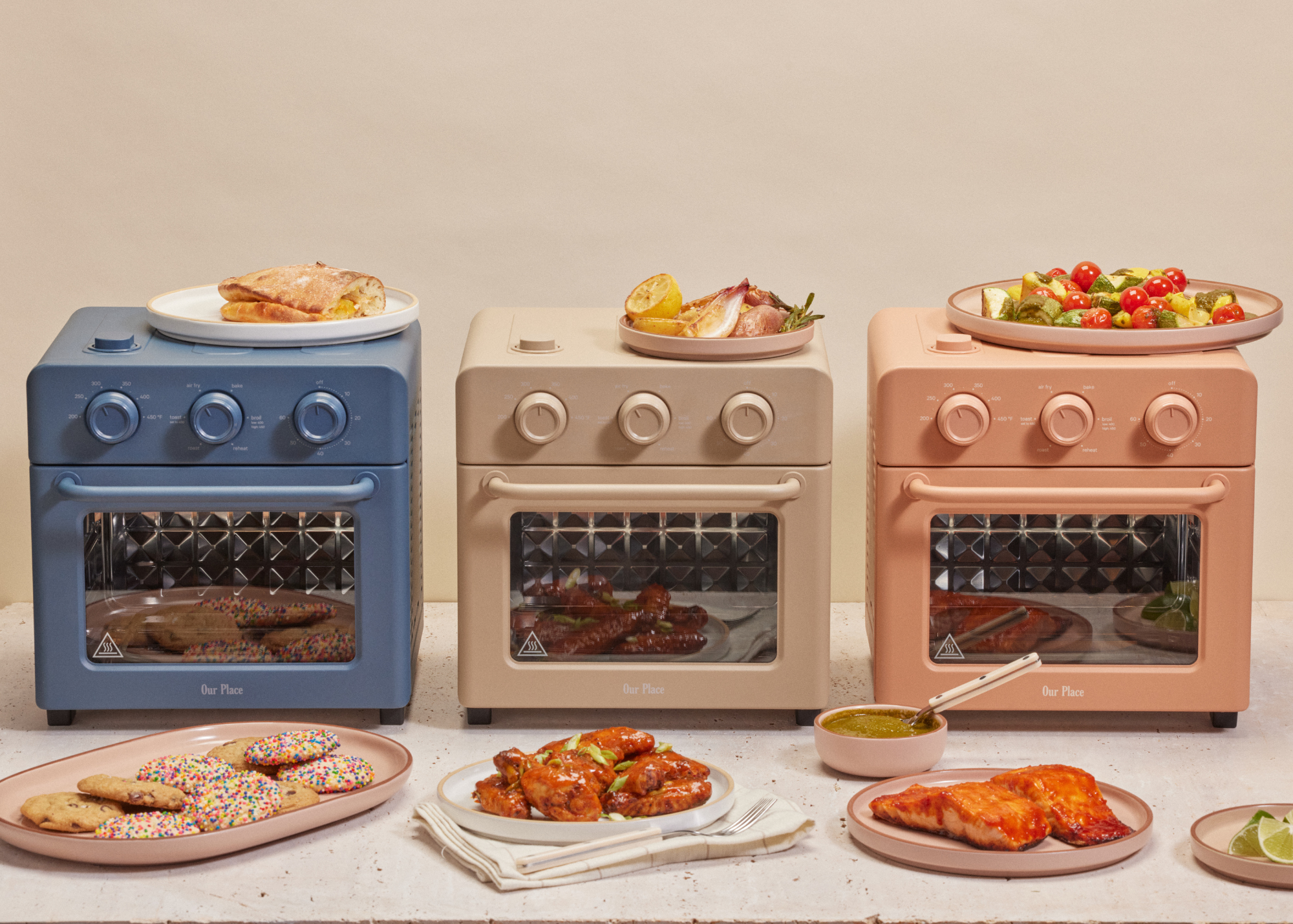 Three Our Place Wonder Ovens (in Blue Salt, Steam, and Spice) surrounded by plates of food