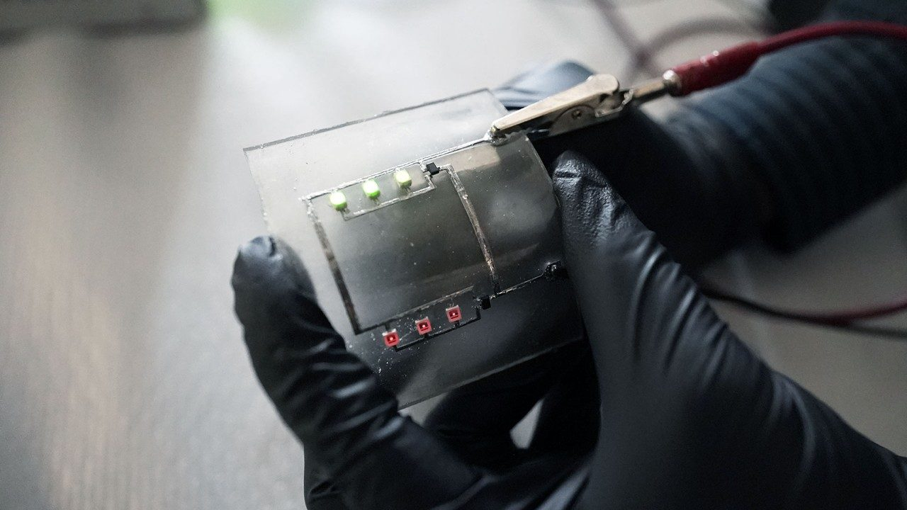 A gloved hand holds a clear, flexible circuit