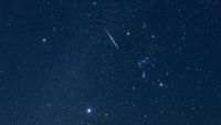 A shooting star is photographed streaking through the night sky through the stars of the constellation Orion.