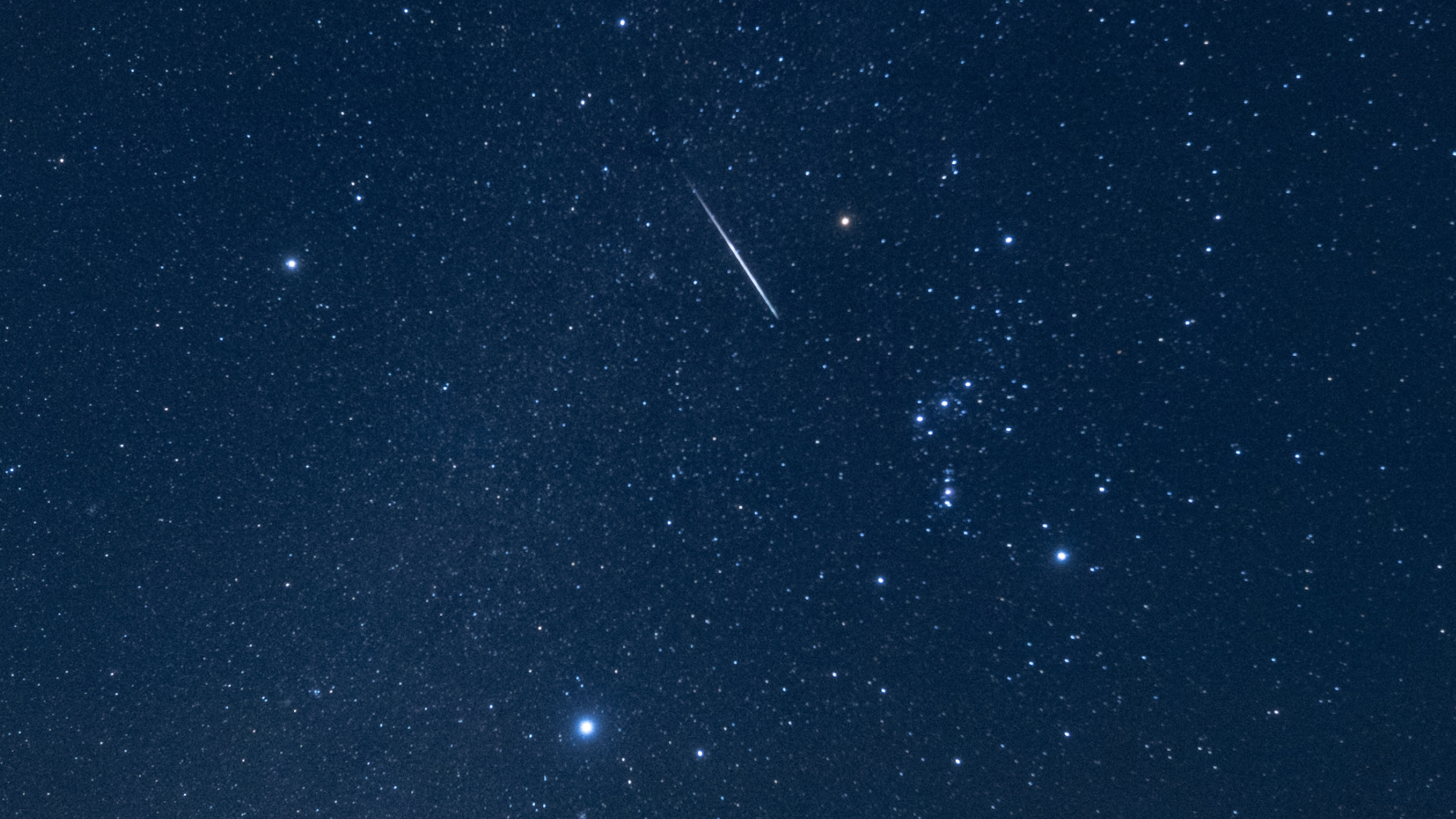 A shooting star is photographed streaking through the night sky through the stars of the constellation Orion.