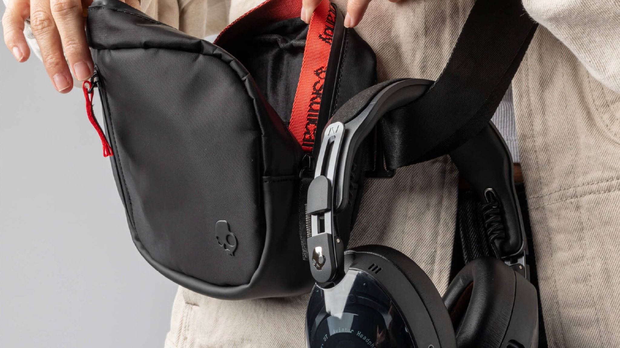 A close-up of the crossbody bag that comes with Skullcandy Aviator 900 ANC headphones. It's black with an embossed skull on it.