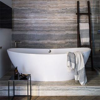 bathroom with stone texture wall and ladder towel rack and bathtub