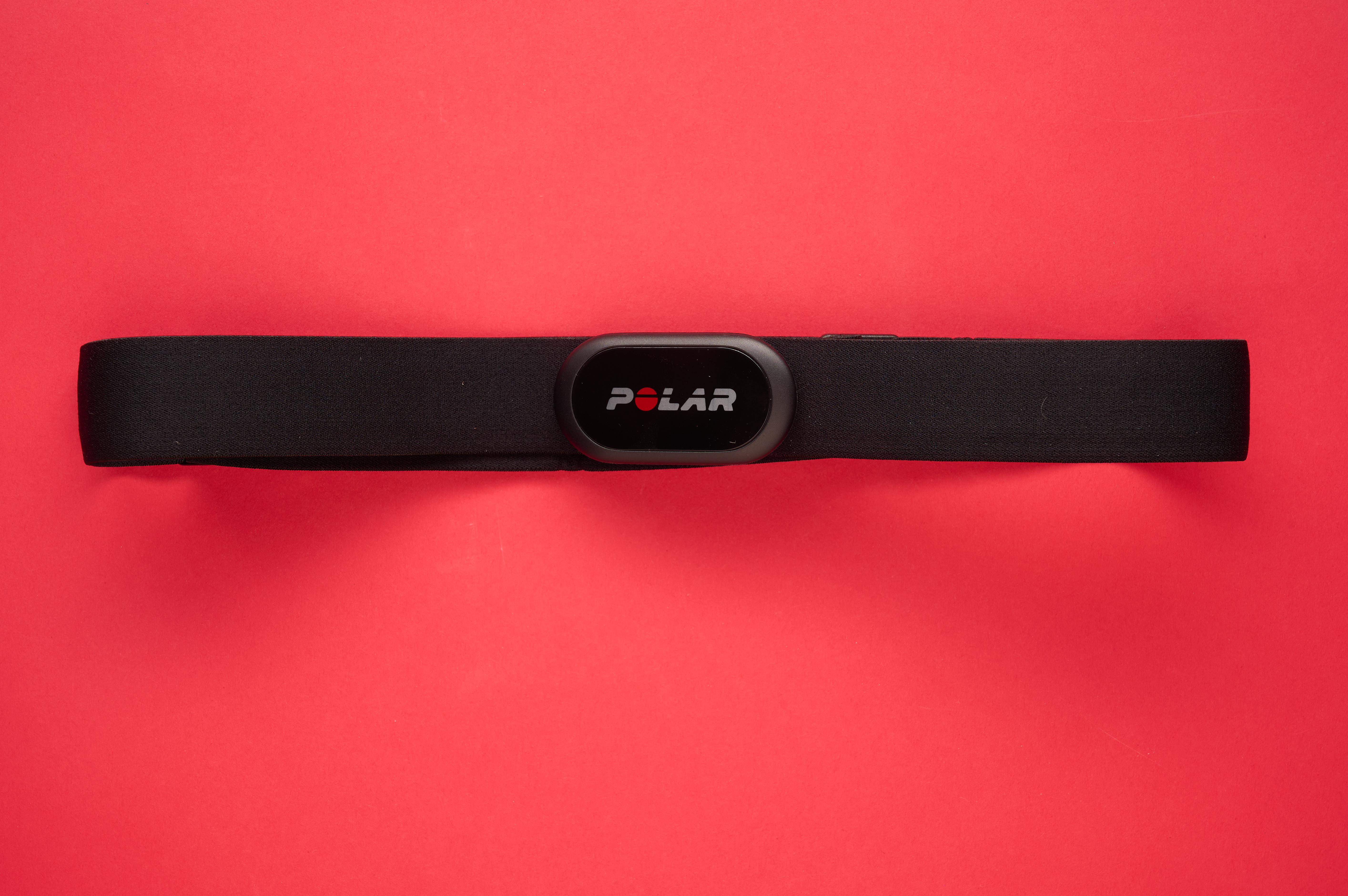 Polar H10 heart rate monitor with its pill like shaped body and distinctive red letter O logo, laid flat on a red background