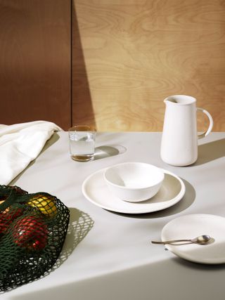 Table setting with crockery, a glass of water and a bag with fruit