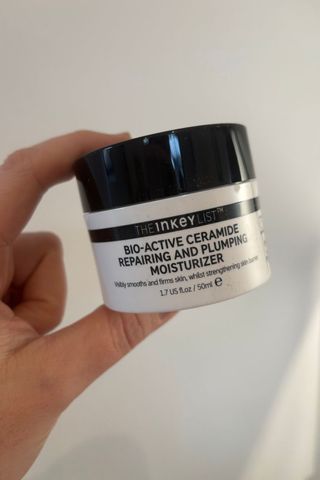 a hand holding a tub of The Inkey List Bio-Active Ceramide Repairing and Plumping Moisturizer