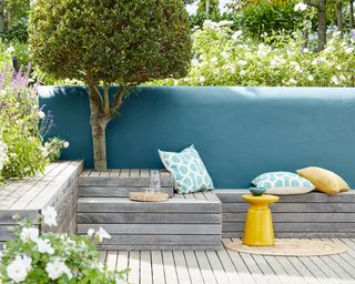 wooden bench-style seating on a deck with a blue painted garden wall