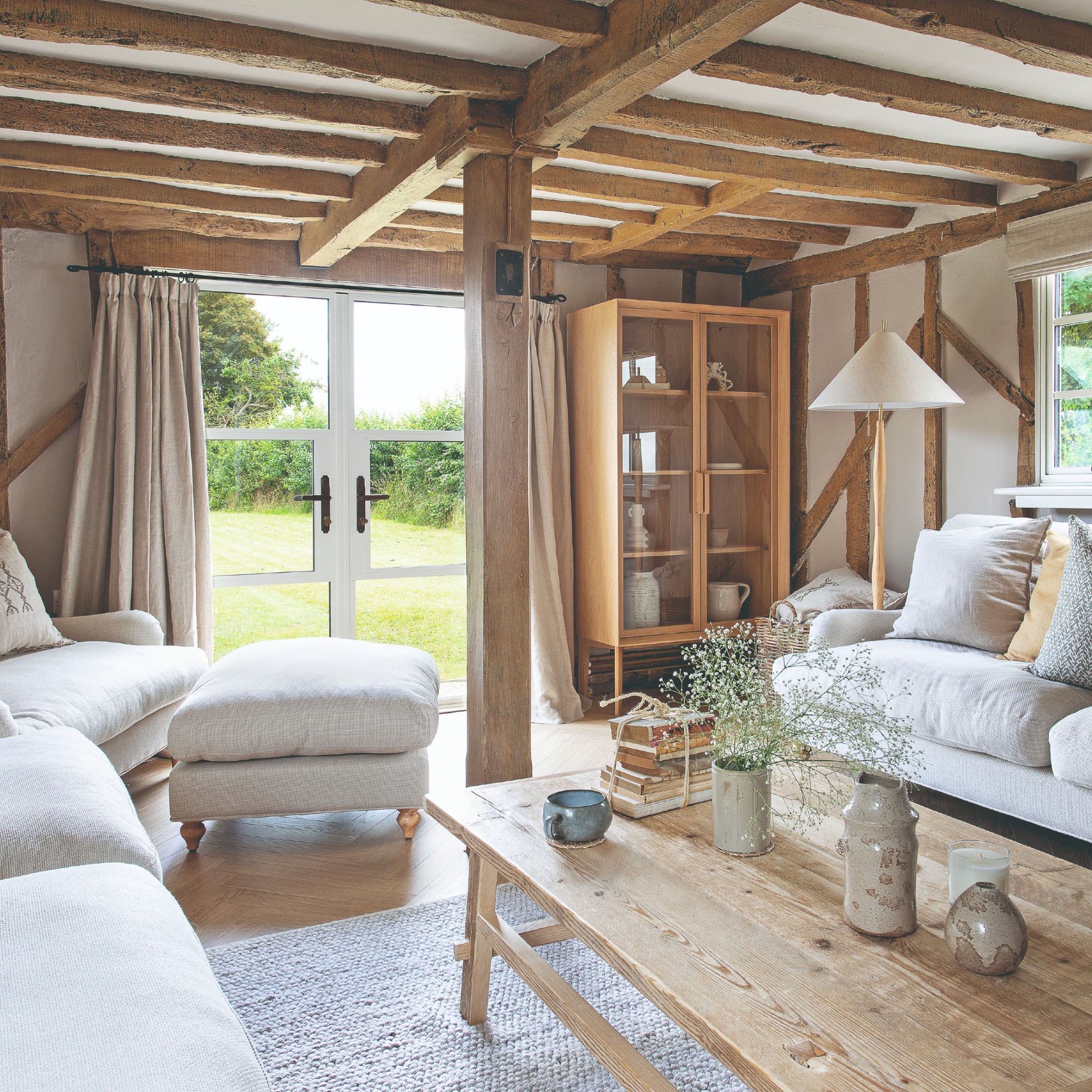 A cottage-style living room with two cream sofas facing each other with a coordinating footstool and a wooden coffee table table in the middle