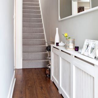 A narrow grey hallway with radiator cover and mirror