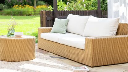 Image of a jute-effect outdoor sofa with white cushions and a matching coffee table on a sunny patio.
