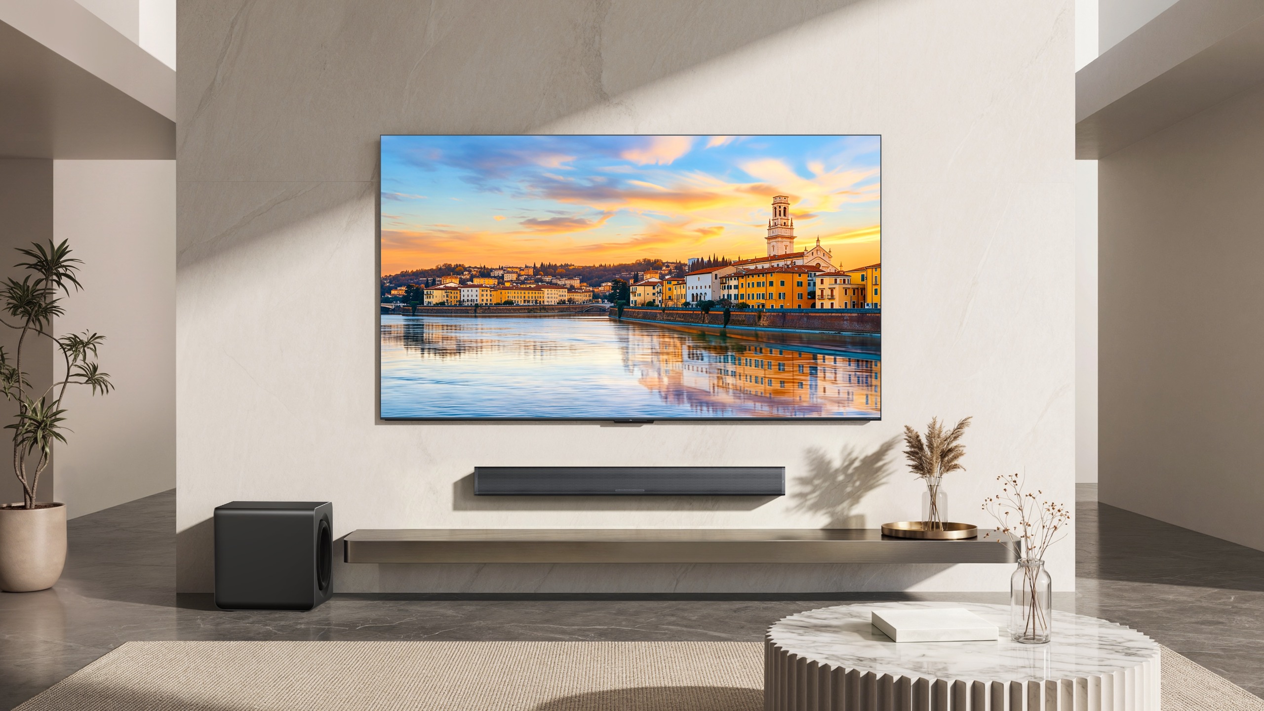 A TCL soundbar wall-mounted below a TV in an airy, modern lounge. On the screen of the TV is a port city at sunset.