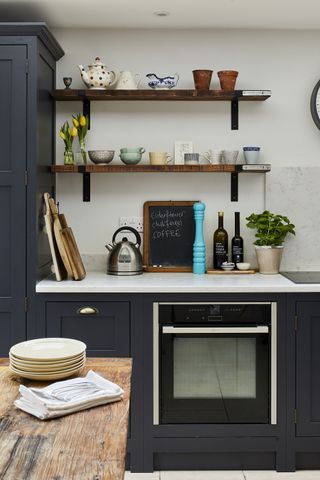 open shelves in a dark blue modern kitchen with ceramics, an oven and kettle