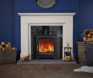 traditional black log burner in large cream stone fireplace with tiled background, stone hearth and log baskets nearby