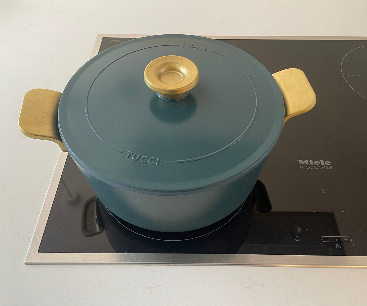 A matte blue round Dutch oven with gold handles on an electric stove top.