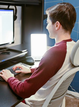 A man sits at a laptop with light next to him