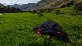 A Sea to Summit Reactor sleeping bag liner lies on a grassy field with hills in the background.