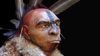 Uma reconstrução de um Neandertal tardio de El Salt. Ele está usando um capacete de penas, um casaco de pele e tem pintura no rosto.