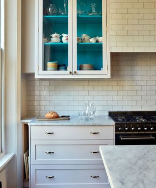 pale pink shaker kitchen with white subway tiles and a glazed wall cabinet