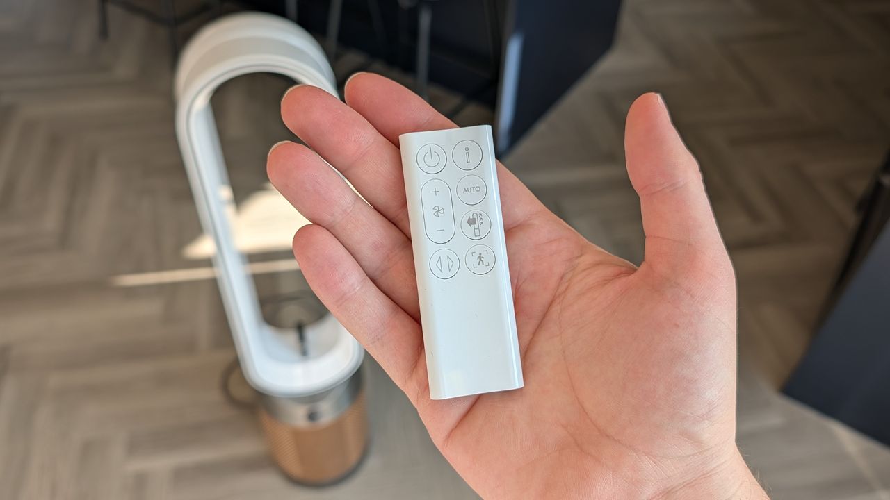 A man's hand holds the Dyson Find+Follow Purifier Cool's remote, while the air purifier is visible in the background.