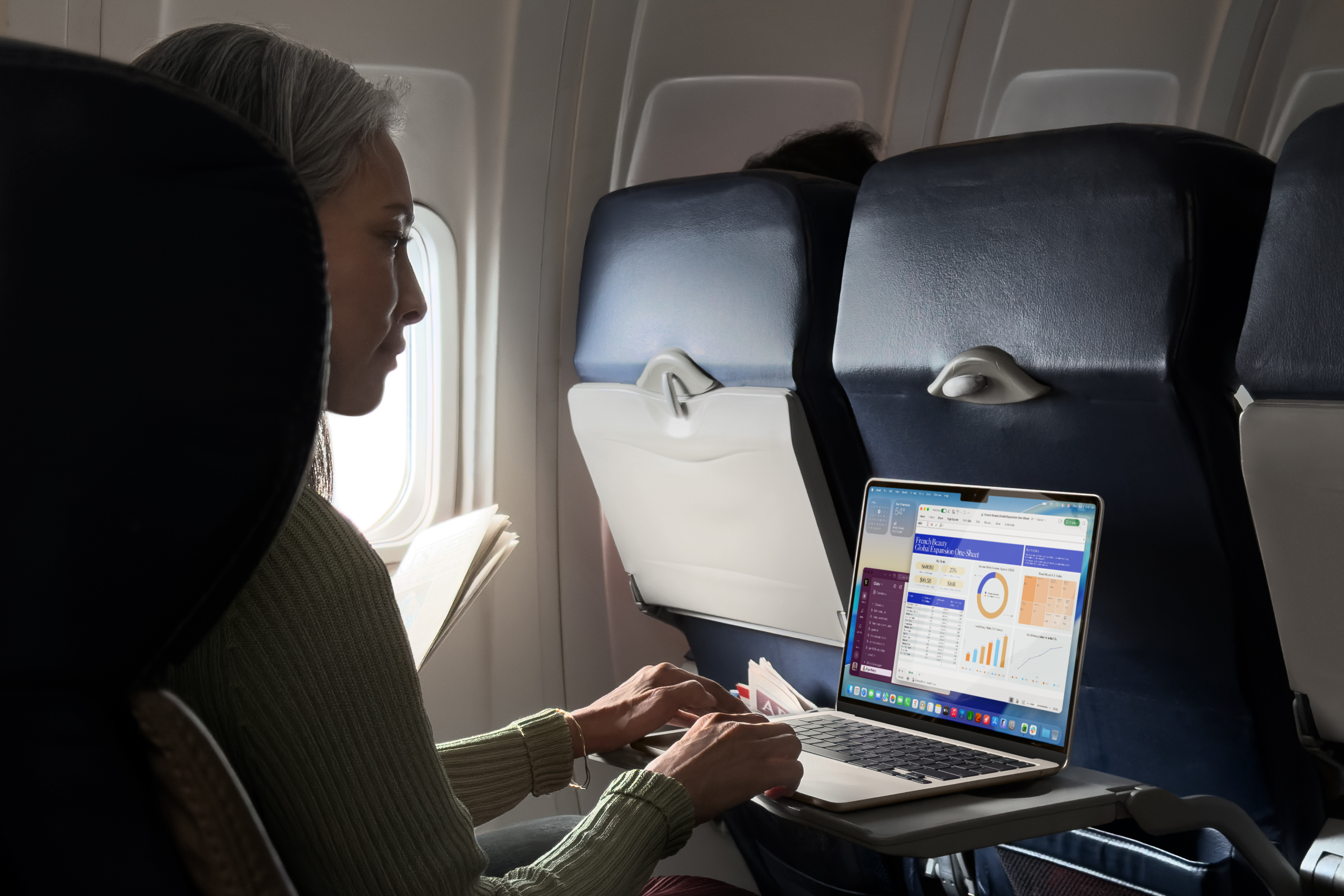 Woman using a MacBook Air on an airplane.