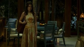 Piper in a long summer dress standing alone in a hotel room looking worried.