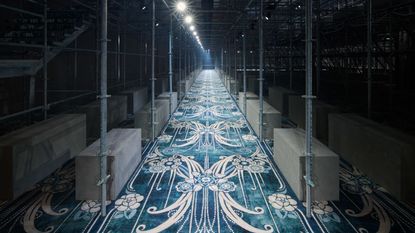 Prada A/W 2025 menswear runway show set featuring scaffolding and patterned carpet