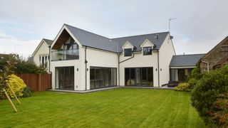 a white and grey spacious family home, with a large garden in the foreground