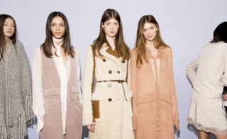 Four women, one in a grey poncho, one in a white shirt under pink corduroy dungarees, one in a cream coat and one in a pink dress