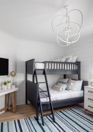 white bedroom with shiplap walls, bunk beds with double bunk below, blue stripe rug, console and chest of drawers