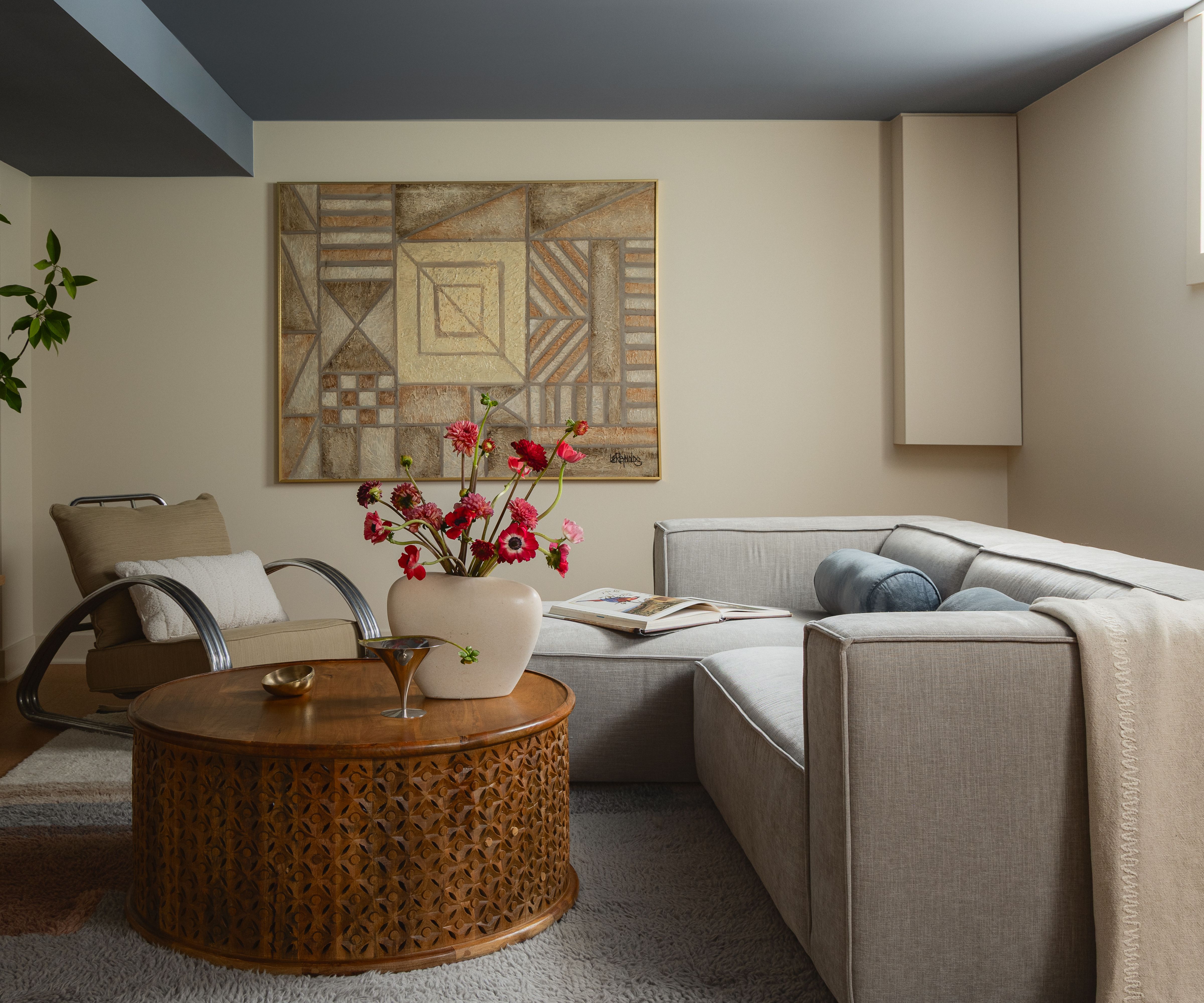 soft beige living room with a blue painted accent ceiling, low modular beige modern sofa, styled with blue lumbar pillows, a throw blanket and a wooden round coffee table styled with a vase of flowers