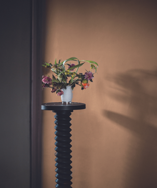 plinth with zig zag edge with vase of flowers against brown wall