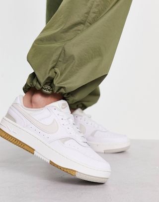 Model wears nike gamma force sneakers in white with olive parachute pants