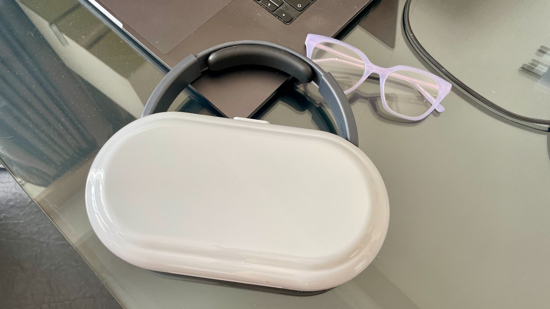 Nothing Headphone (1) Pro with the case on a shiny black and glass table, next to a pair of glasses