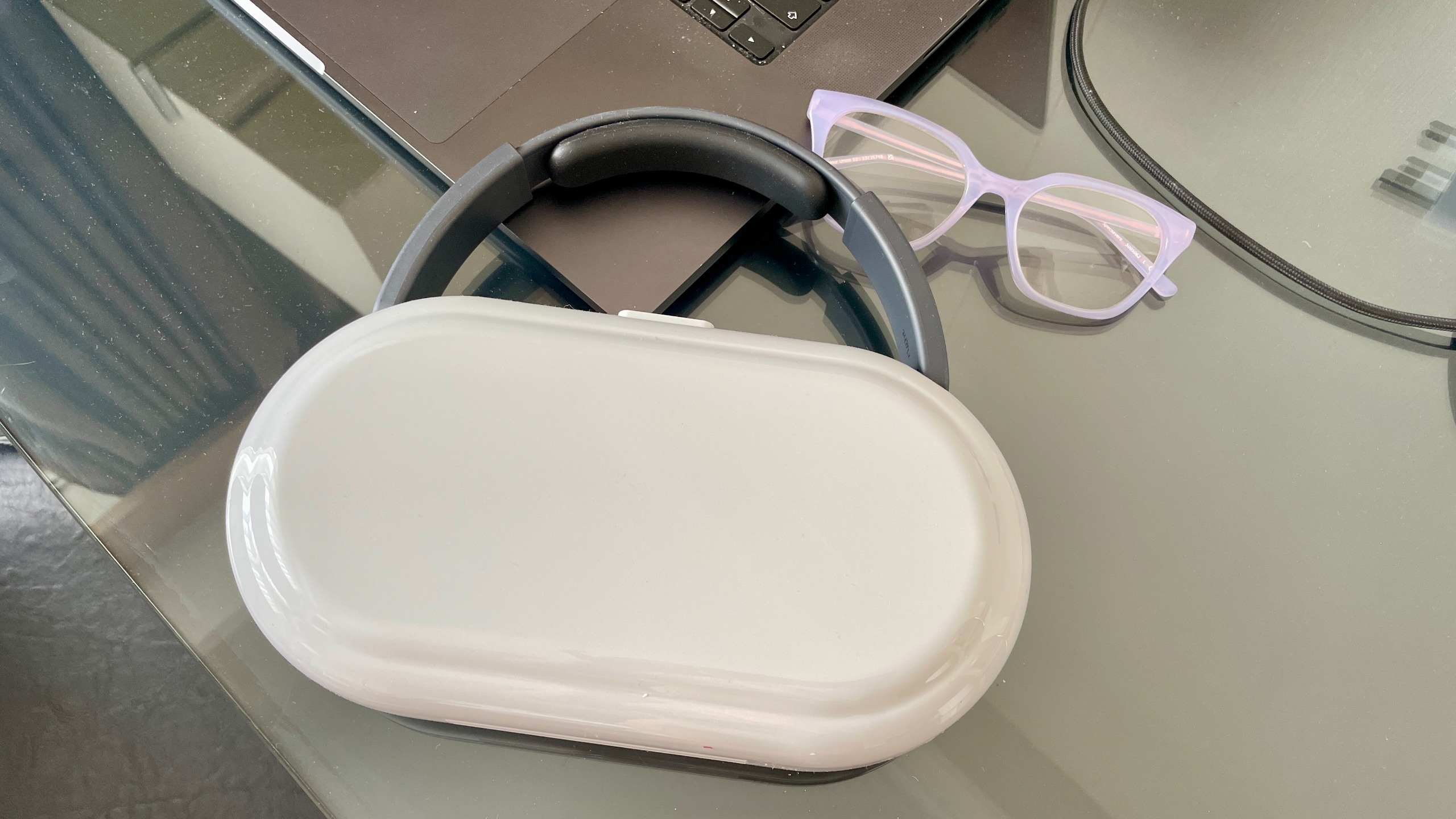 Nothing Headphone (1) Pro with the case on a shiny black and glass table, next to a pair of glasses