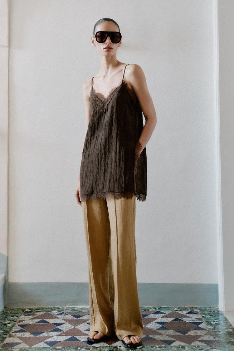 Woman is wearing camisole and trousers and flip flops.