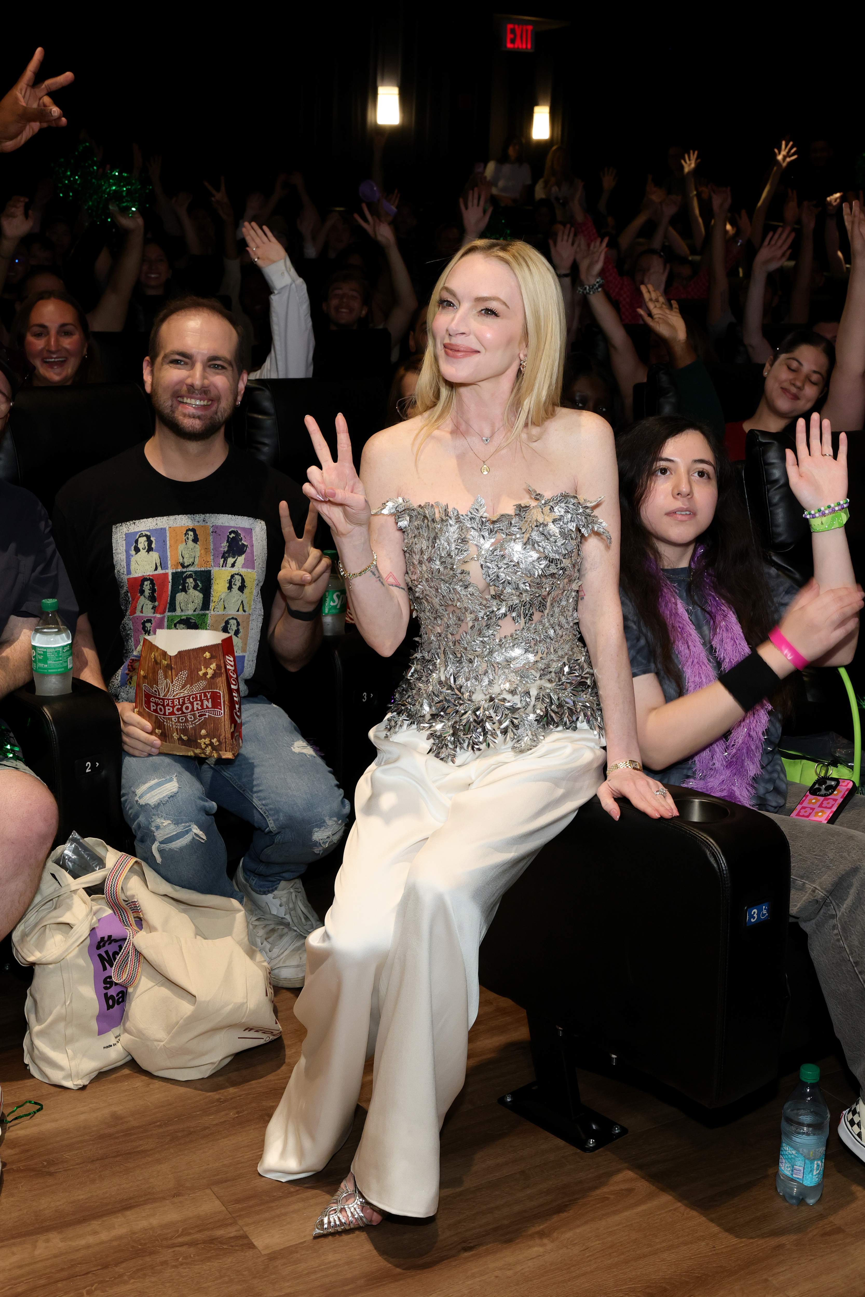 Lindsay Lohan wears a metallic strapless top, white pants, a Cartier watch, and carries an Hermes Kelly bag
