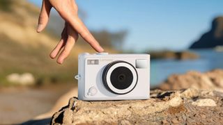 Lenovo C55 lifestyle image of camera on rocks in front of landscape with hand touching mode dial 