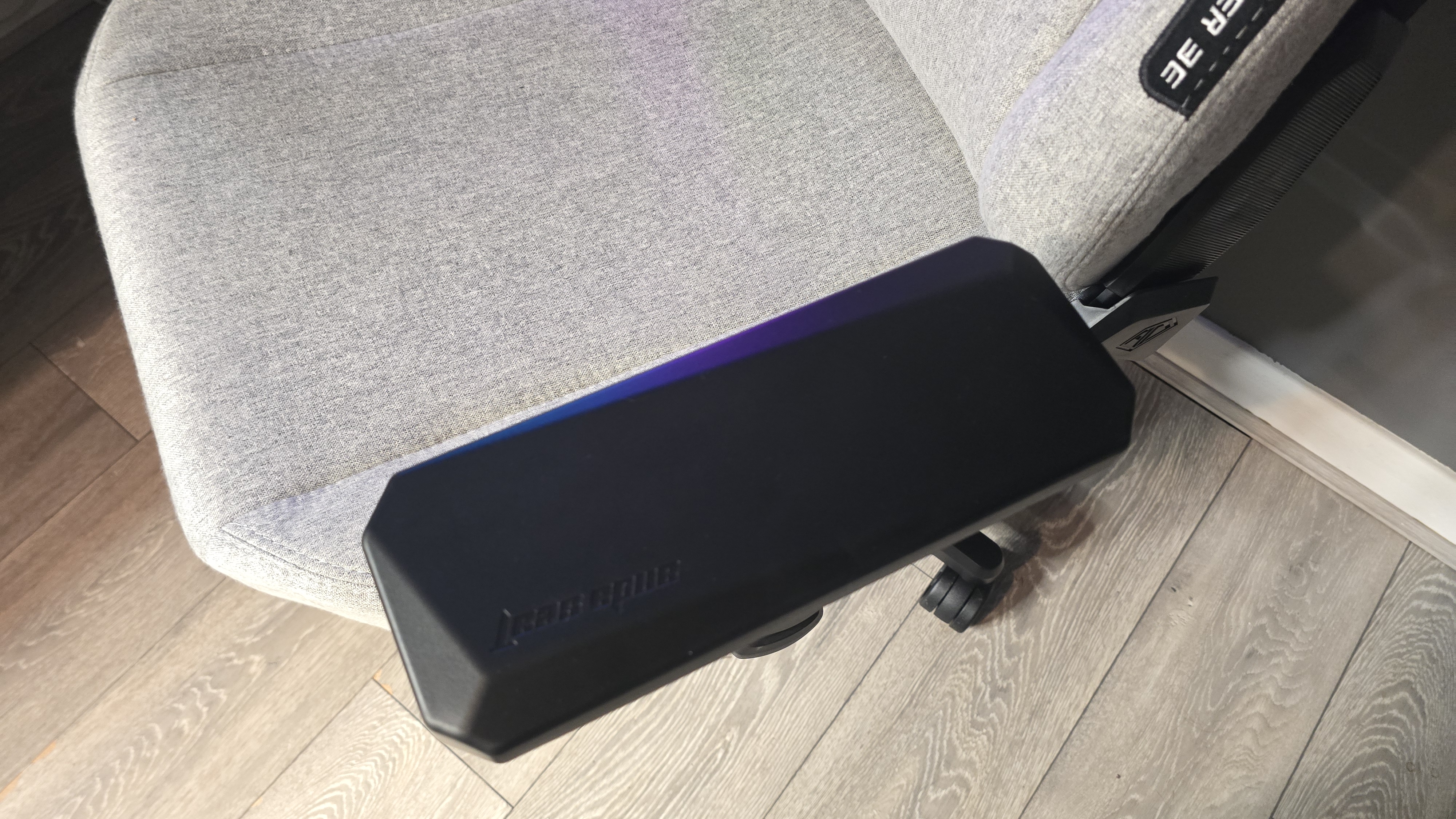 A grey gaming chair, with focus on the left armrest