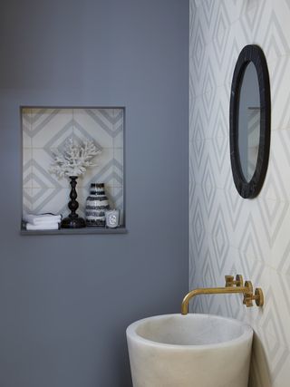 blue powder room with blue patterned tiles on wall and alcove, round basin, brass taps, mirror