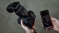 Canon EL-5 flashgun on camera being held in someone's hand, with a smartphone with the app in the other hand