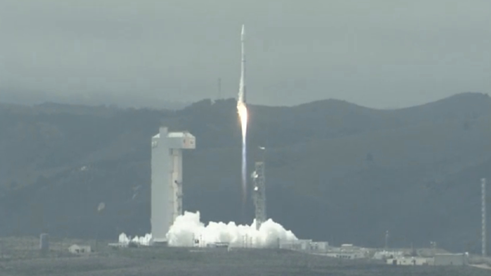 A rocket blasts off from a launch pad near a hillside