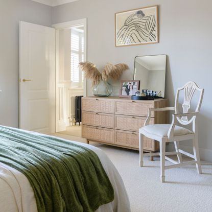 White bedroom with bohemian features, including a rattan chest of drawers and wooden chair