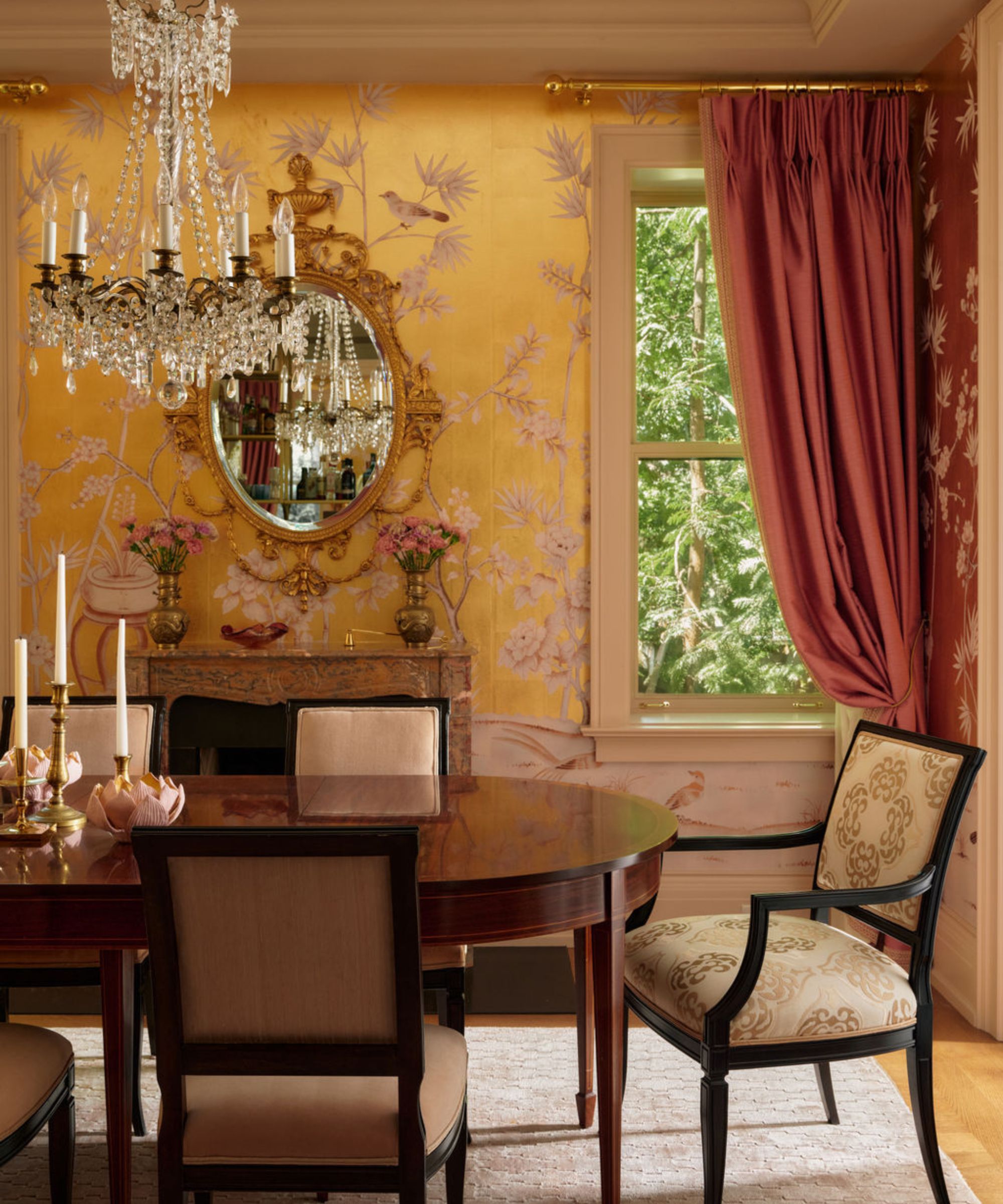 a gold wallpapered dining room with original fireplace, pink drapes and an antique wooden table