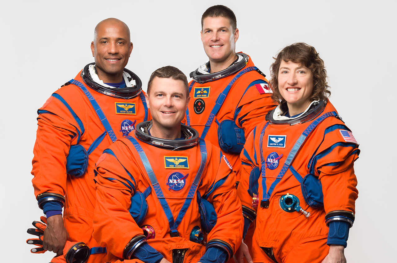 four astronauts stand in a group with their spacesuits on, smiling