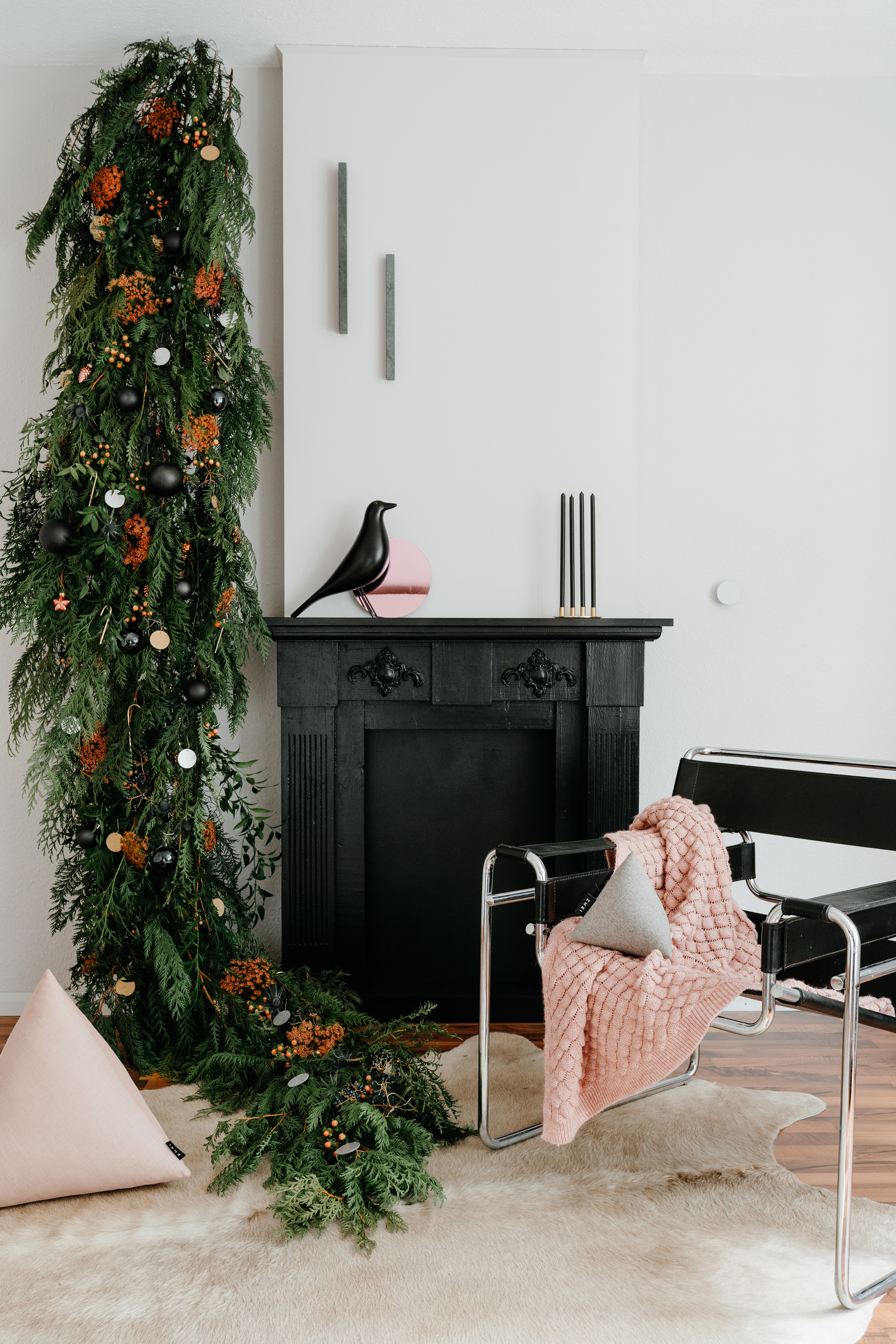 A living room with a black fireplace, an accent chair, and a bough of seasonal foliage on draped from the ceiling down the wall
