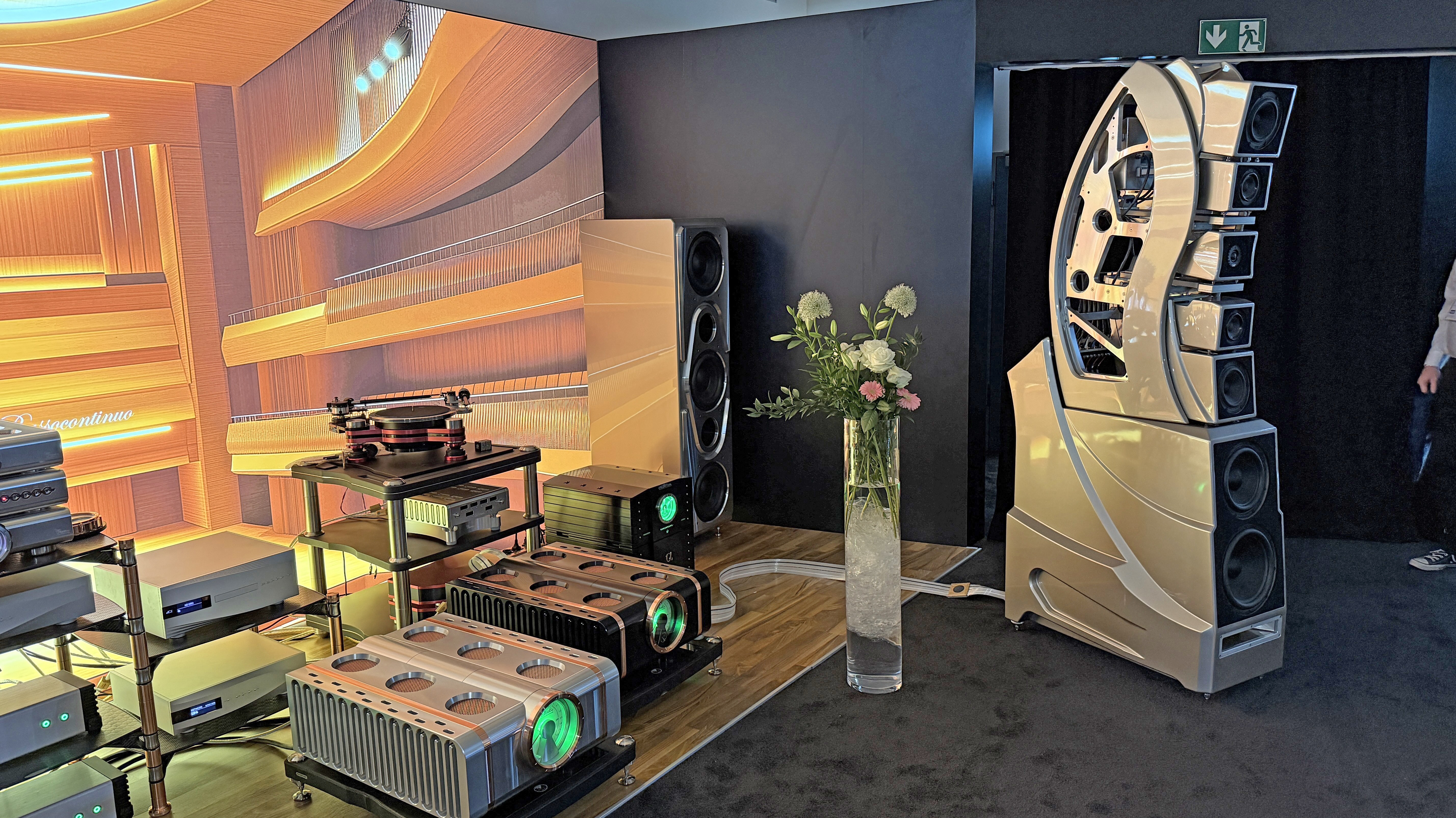 A very large speaker with a subwoofer behind it, next to several large amplifiers