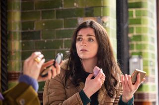 Áine (Aisling Bea) applying make-up with a compact mirror while talking to her sister Shona (Sharon Horgan), who's just out of shot